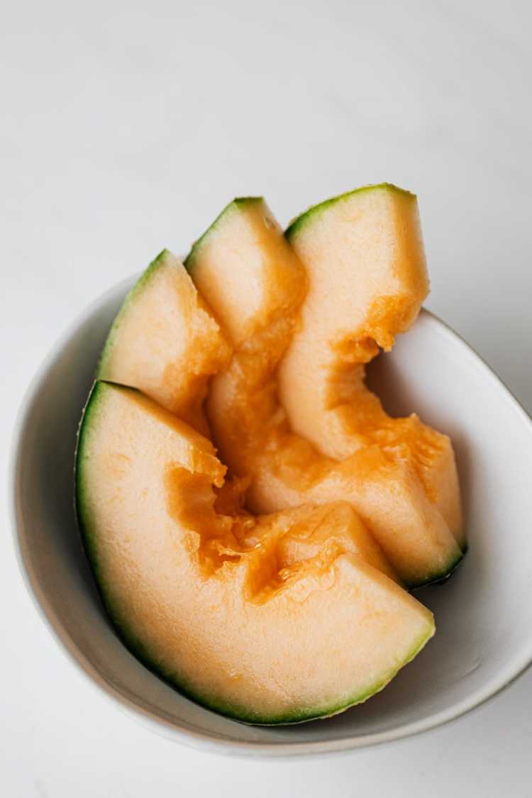 From above of sliced ripe juicy cantaloupe melon in bowl placed on white table